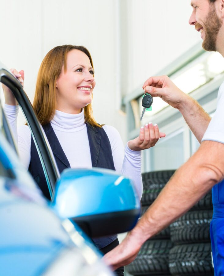 Female client and mechanic in auto workshop or MOT with car for service inspection